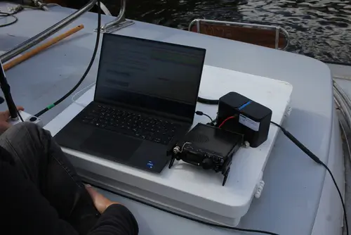 schwarzer Laptop, Funkgerät, Akkupack auf Deck eines Bootes